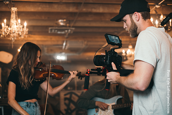 Ein Mann filmt eine Frau, während sie Geige spielt.