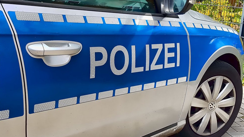 KI generiert: Das Bild zeigt die Seitenansicht eines deutschen Polizeiautos mit dem Schriftzug "POLIZEI" auf der blauen Tür. Ein Teil eines Reifens und die Autotür sind sichtbar.