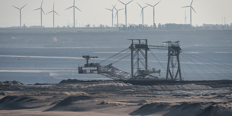 KI generiert: Das Bild zeigt einen großen Schaufelradbagger in einem Tagebau vor einer Reihe von Windkraftanlagen im Hintergrund. Der Kontrast zwischen der Kohleförderung und den Windrädern symbolisiert den Konflikt zwischen traditioneller und erneuerbarer Energieerzeugung.