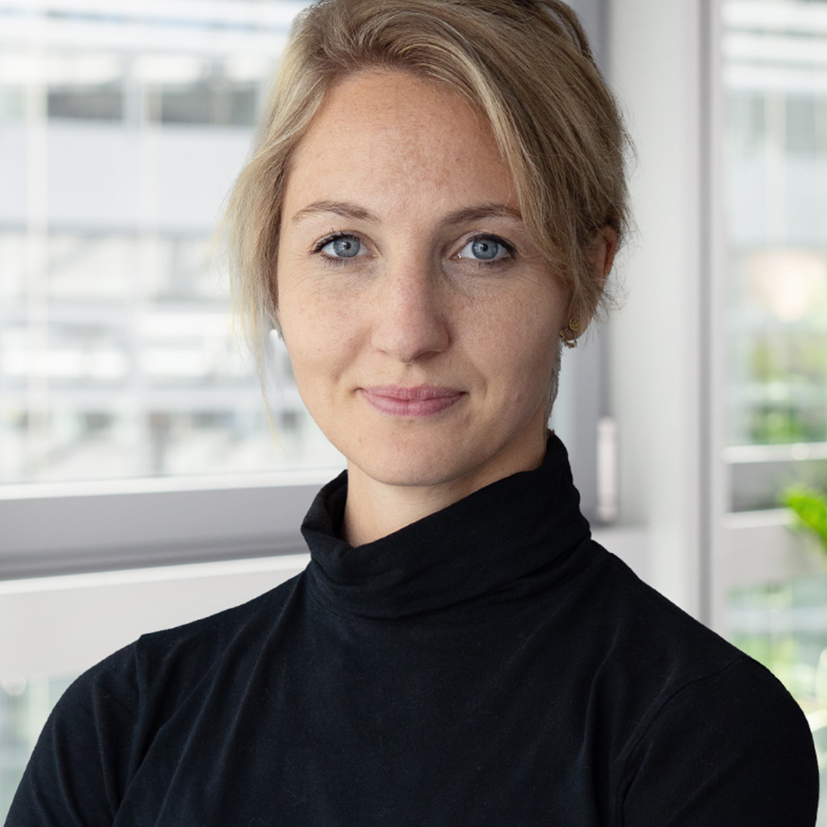 KI generiert: Das Bild zeigt eine Person mit blonden Haaren, die in einem schwarzen Rollkragenpullover vor einem Fenster steht. Der Fokus des Bildes liegt auf dem Porträt der Person.