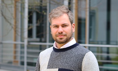 Markus Wulff steht vor einer Gebäudestruktur und schaut in die Kamera.