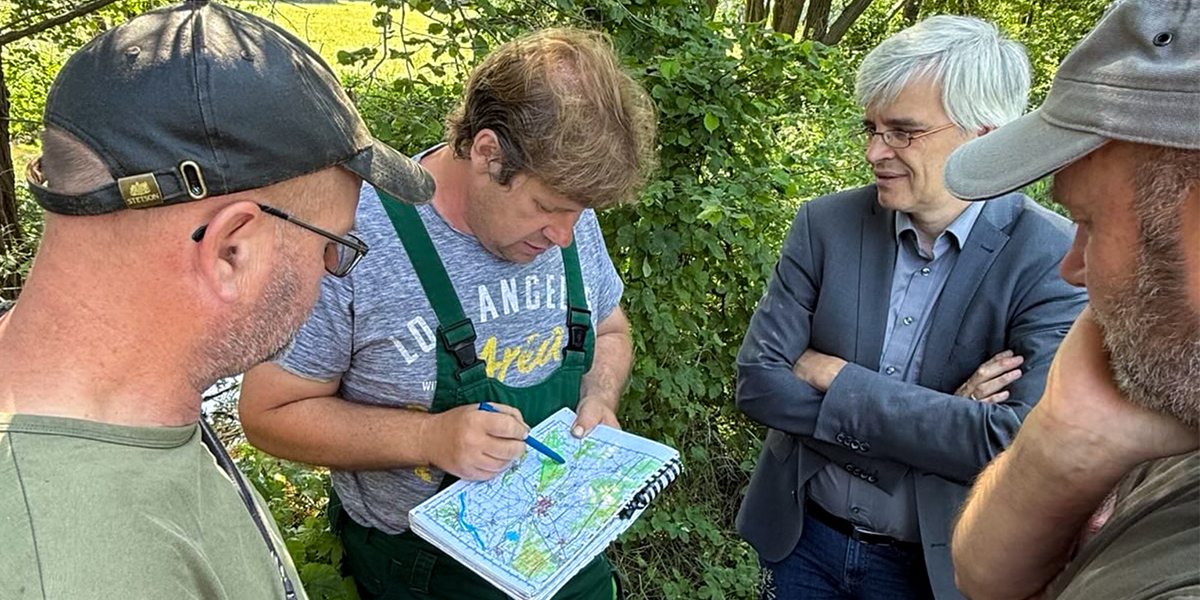 KI generiert: Eine Gruppe von vier Männern steht in einem grünen, bewaldeten Gebiet. Einer von ihnen zeigt auf eine Karte, während die anderen aufmerksam zuschauen.