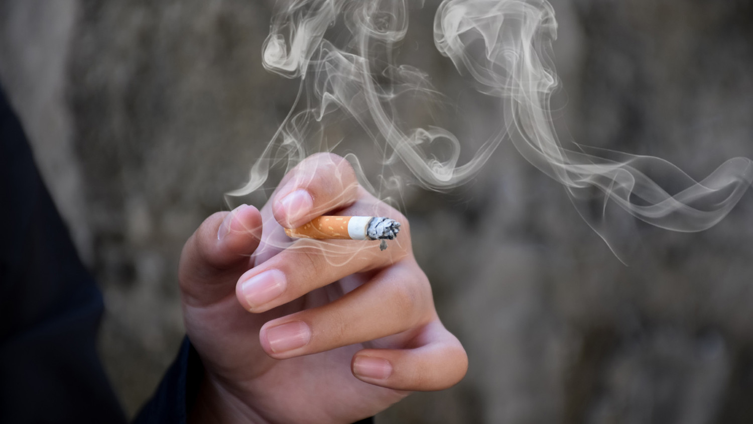 KI generiert: Das Bild zeigt eine Hand, die eine brennende Zigarette hält, aus der Rauch aufsteigt. Der Hintergrund ist unscharf und hebt die Hand mit der Zigarette hervor.