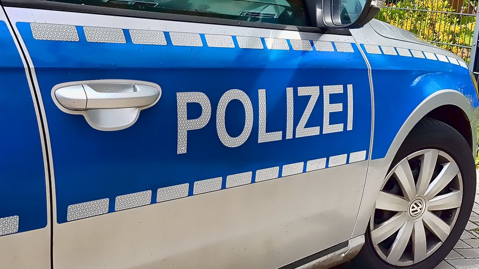 KI generiert: Das Bild zeigt die Seitenansicht eines deutschen Polizeiautos mit dem Schriftzug "POLIZEI" auf der blauen Tür. Ein Teil eines Reifens und die Autotür sind sichtbar.