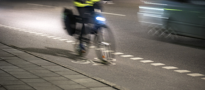 KI generiert: Das Bild zeigt einen Radfahrer, der in der Nacht mit eingeschaltetem Vorderlicht auf einem Fahrradweg fährt. Die Szene ist in Bewegung und auf einer Straße erkennbar.