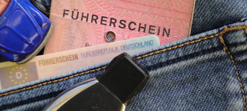 KI generiert: Das Bild zeigt zwei deutsche Führerscheine, einen älteren rosafarbenen und einen neueren, plastikartigen, die aus der Gesäßtasche einer Jeans herausragen. Neben den Führerscheinen ist ein Modellauto sichtbar.