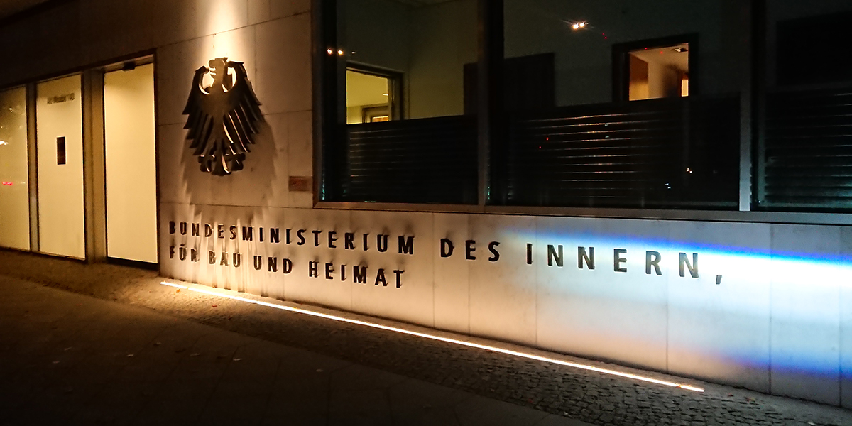 KI generiert: Das Bild zeigt den Eingang des Bundesministeriums des Innern, für Bau und Heimat in Deutschland. Der Schwerpunkt liegt auf der Gebäudeaufschrift und dem Bundesadler-Emblem neben dem Eingang.