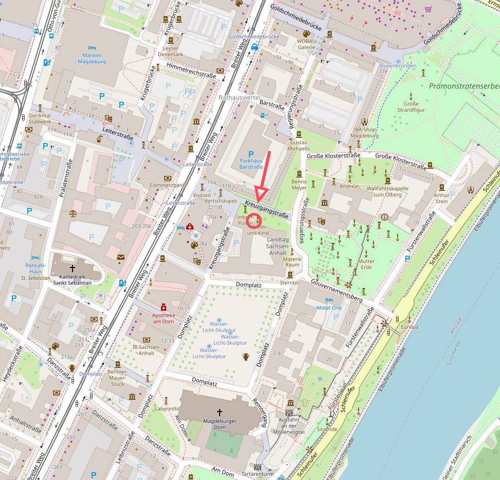 KI generiert: Das Bild zeigt eine Stadtkarte des Zentrums von Magdeburg, auf der verschiedene Straßennamen und Gebäude markiert sind. Ein roter Pfeil weist auf die Kreuzgangstraße in der Nähe des Elbufers hin.
