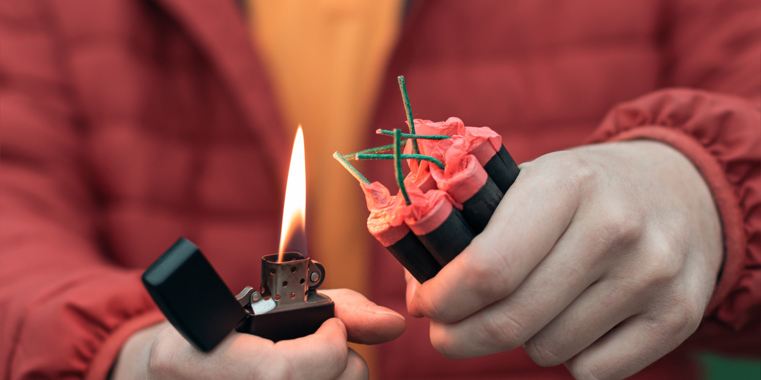KI generiert: Das Bild zeigt eine Person, die dabei ist, eine Gruppe von zusammengesteckten Feuerwerkskörpern oder Böllern mit einem Feuerzeug zu entzünden. Die Szene fokussiert auf die Hände und den potenziell riskanten Moment des Zündens.