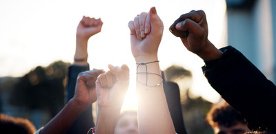 KI generiert: Das Bild zeigt mehrere in die Luft gestreckte, geballte Fäuste, die ein Gefühl von Einheit und Stärke vermitteln. Im Hintergrund ist ein heller Himmel zu sehen.