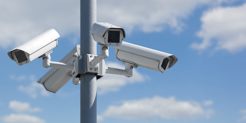 KI generiert: Das Bild zeigt mehrere Überwachungskameras, die an einem Mast befestigt sind, vor einem Hintergrund eines blauen Himmels mit wenigen Wolken. Der Hauptinhalt ist die Überwachungstechnologie.